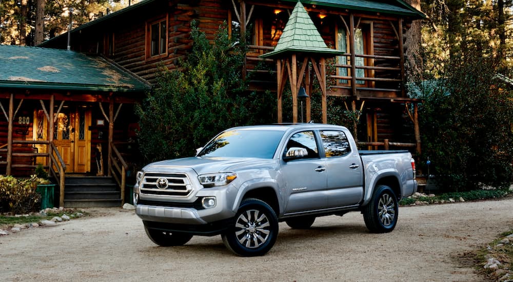 A silver 2021 Toyota Tacoma is shown parked in front of a log cabin.