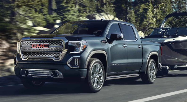 A grey 2021 GMC Sierra 1500 is towing a boat down a tree lined road.