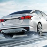 A white 2021 Nissan Altima is shown driving on a snowy road after winning a 2021 Nissan Altima vs 2021 Toyota Camry comparison.