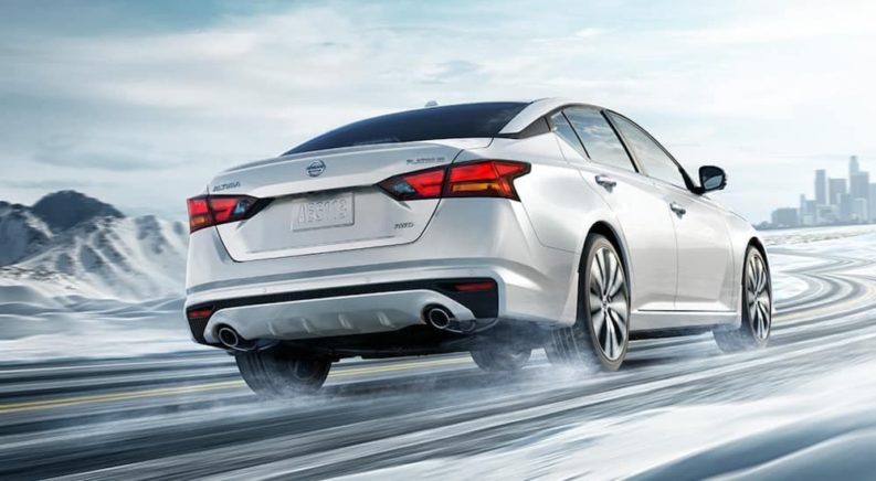 A white 2021 Nissan Altima is shown driving on a snowy road after winning a 2021 Nissan Altima vs 2021 Toyota Camry comparison.