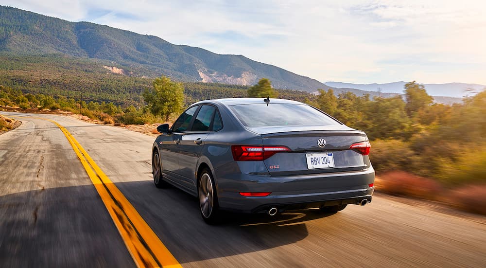 A grey 2021 Volkswagen Jetta GLI is shown from the rear driving down an empty road.