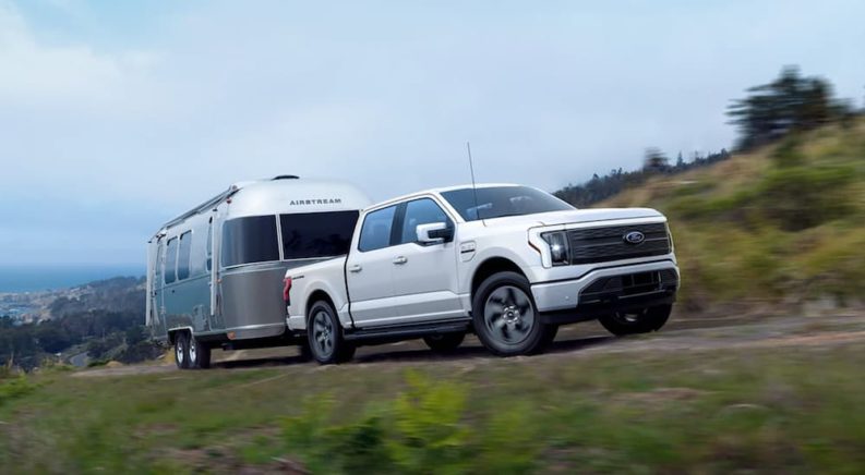 A white 2022 Ford Lightning is towing an Airstream after leaving a Ford Lightning dealership.