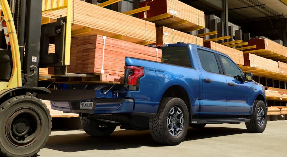 A blue 2022 Ford Lightning is shown carrying wood at a lumber yard.