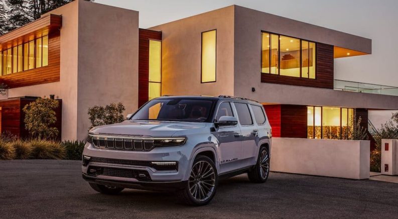 A silver 2021 Grand Wagoneer is parked outside of a modern house after winning a 2022 Grand Wagoneer vs 2021 Lexus GX comparison.