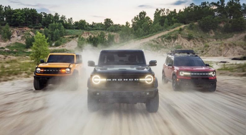 A yellow, a black, and a red 2021 Ford Bronco are shown driving down a dirt path.