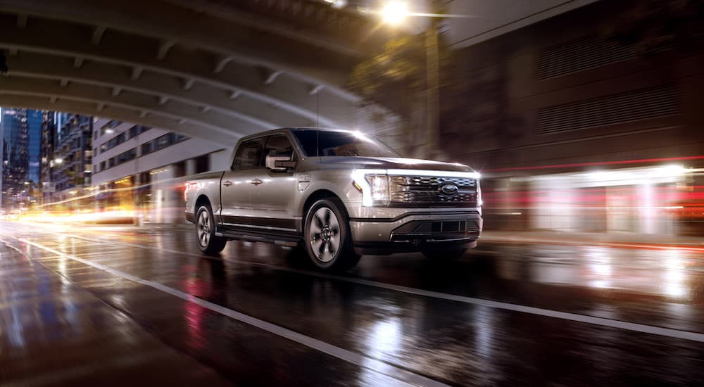 A 2022 Ford F-150 Lightning Platinum is shown driving through a city at night.