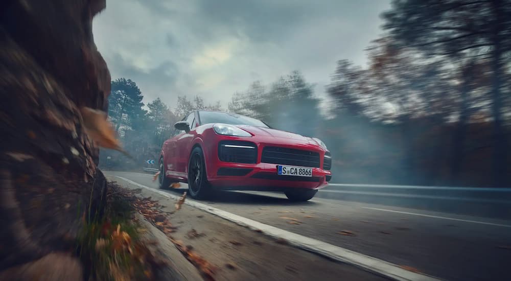 A red 2021 Porsche Cayenne is shown from a low angle driving down a road.