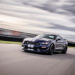 A blue 2019 Ford Mustang Shelby GT350 is shown driving around a track on a cloudy day.