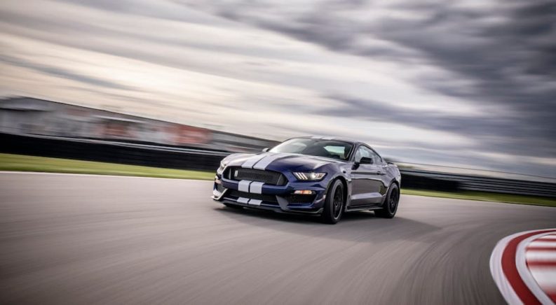 A blue 2019 Ford Mustang Shelby GT350 is shown driving around a track on a cloudy day.