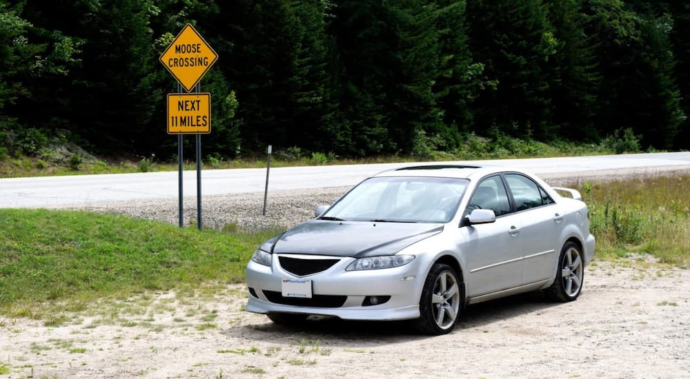 A silver 2003 Mazda6 is parked in front of a moose crossing sign.