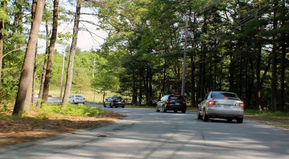 A line of Mazda6 cars are shown driving on a tree lined road.