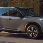 A grey 2021 Nissan Rogue is parked on a city street outside of a brick building after leaving a Nissan dealer.