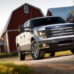 A black 2011 Ford F-150 Lariat is shown parked in front of a barn and silo.