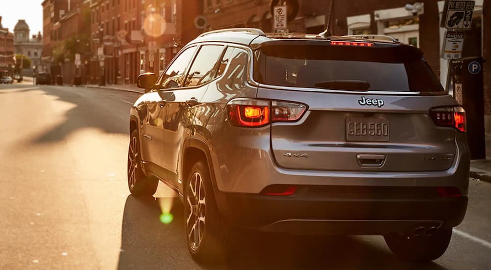 A silver 2020 Jeep compass is driving down a city street at sunset.