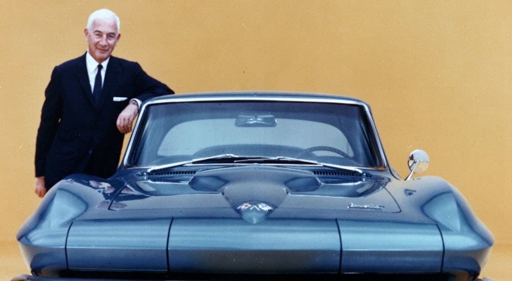 Zora Arkus-Duntov is shown leaning against a dark blue 1966 Chevy Corvette.