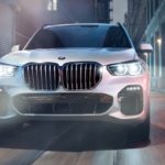 A white 2021 BMW X5 is shown from the front driving through a city at night.