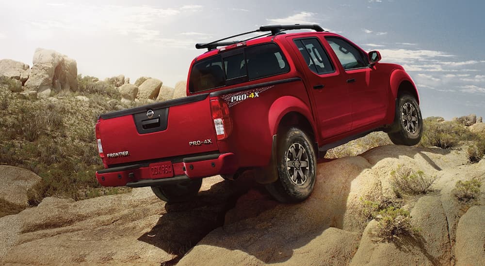 A red 2021 Nissan Frontier Pro 4x is shown from the rear off-roading on a rock pile.