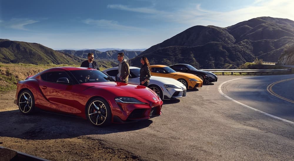 A reed, a white, a yellow, and a blue 2021 Toyota GR Supra are parked in a row around a corner.