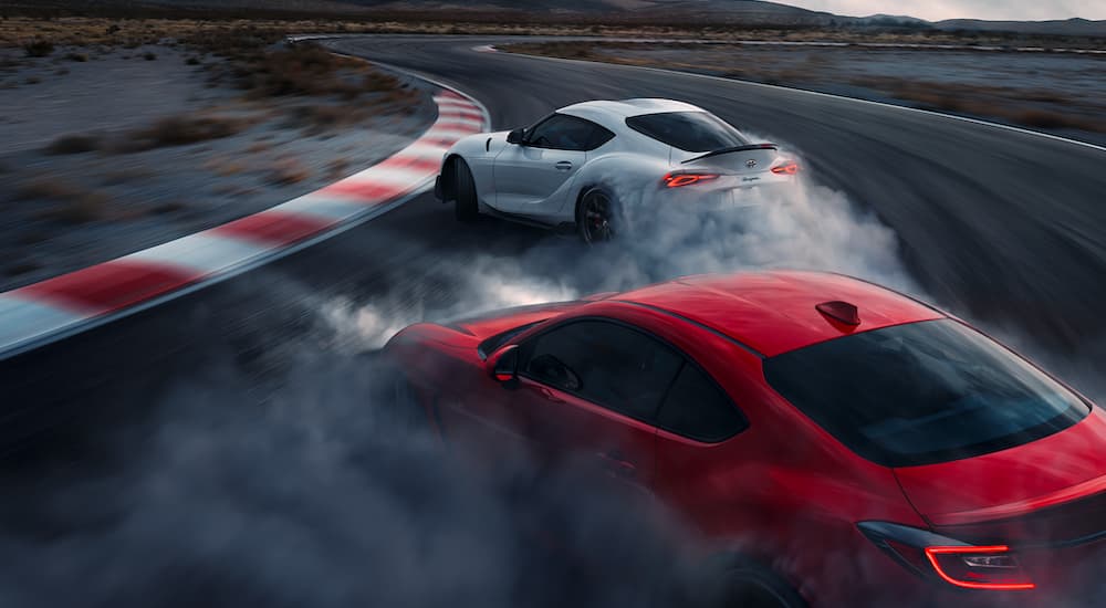 A white 2022 Toyota GR Supra A91 CF Edition is tandem drifting around a track with a red 2022 Toyota GR 86.