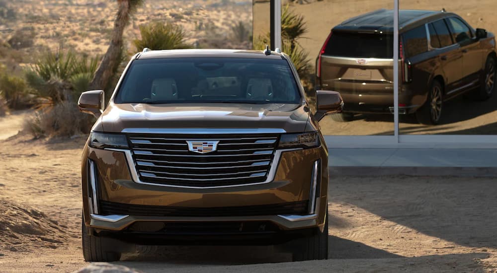 A gold 2021 Cadillac Escalade is shown from the front parked in front of a modern house in the desert.
