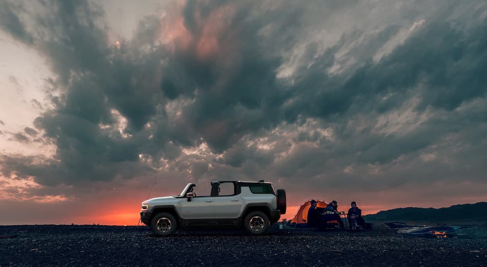 A white 2023 GMC Hummer EV SUV is shown at a camp site during a sunset.