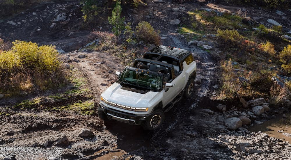 A white 2023 GMC Hummer EV SUV is shown from a high angle driving on a muddy path.