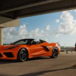 An orange 2022 Chevy Corvette is shown parked next to a guard rail and woman.