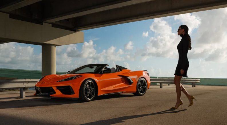 An orange 2022 Chevy Corvette is shown parked next to a guard rail and woman.