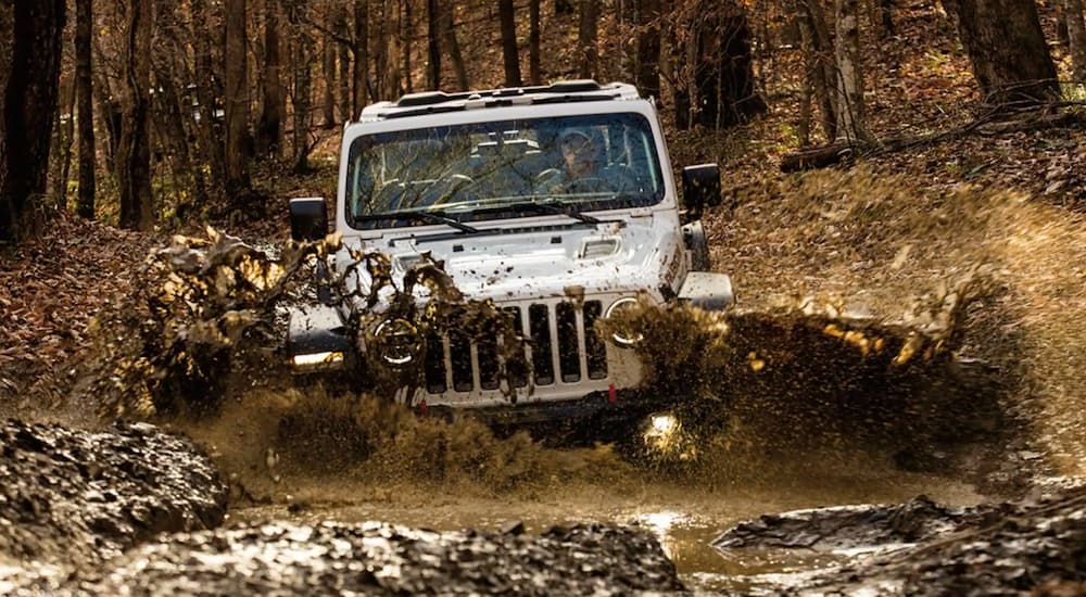 A white 2022 Jeep Wrangler Xtreme Recon is shown from the front off-roading through a mud puddle after leaving a Jeep Dealership.