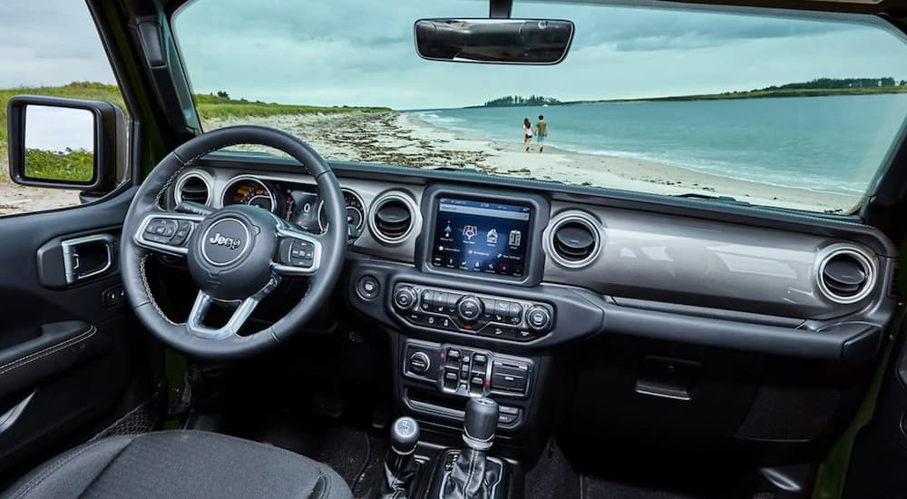 The black interior of a 2022 Jeep Wrangler shows the steering wheel and infotainment screen.