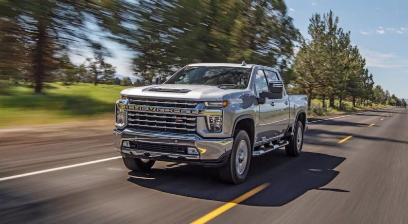 One of the most popular pre-owned Chevy trucks, a silver 2021 Chevy Silverado 2500 HD Z71, is shown driving down a tree-lined road.