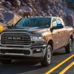 A brown 2020 Ram 2500 Laramie Longhorn is shown driving past a rock face after leaving a Ram dealership in NJ.