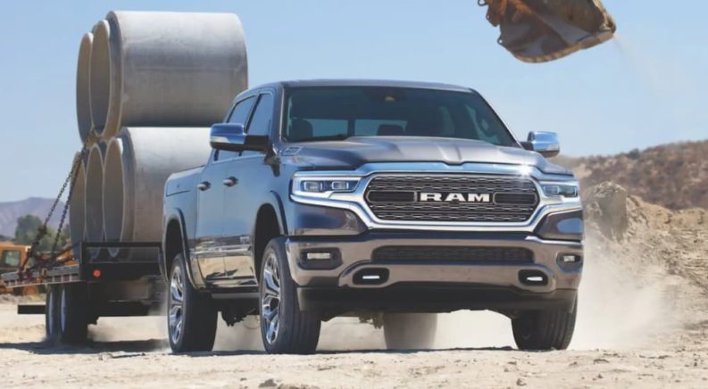 A blue 2021 Ram 1500 is shown towing a flatbed loaded with construction materials.