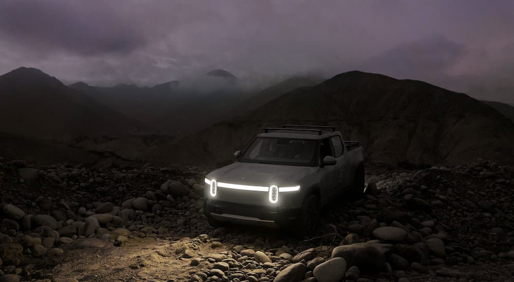 A silver 2022 Rivian R1T is shown with its headlights illuminated in the dark.