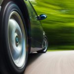A black car is shown driving from a low angle after leaving a used car dealer.