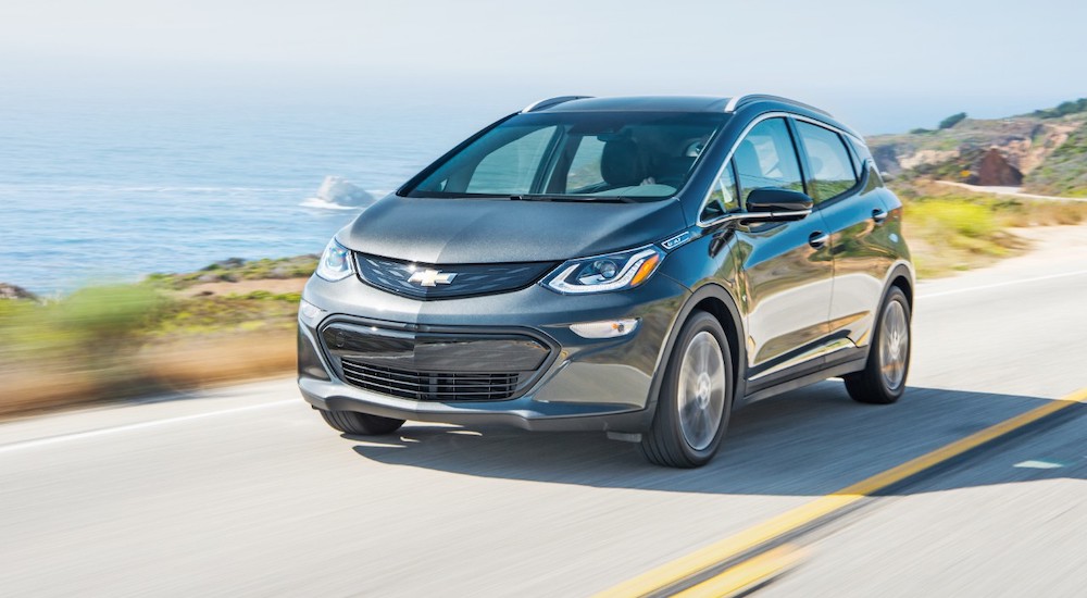 A grey 2019 Chevy Bolt EV is driving on a road next to the ocean.
