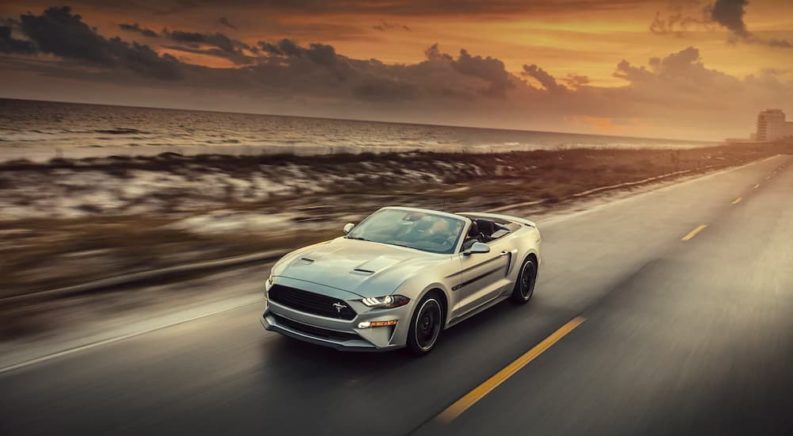 A silver 2021 Ford Mustang is driving past the ocean after winning a 2021 Ford Mustang vs 2021 Chevy Camaro showdown.