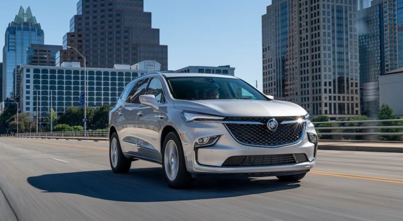 A silver 2022 Buick Enclave Avenir is shown driving away from a city.