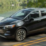 A black 2022 Buick Encore is shown from the side driving on an open road past a lake.