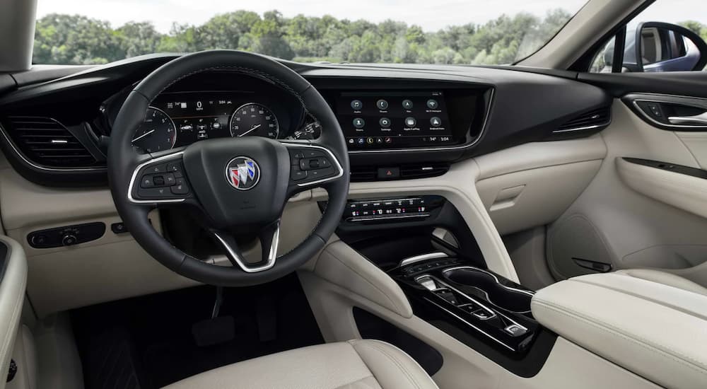 The black and tan interior of a 2022 Buick Envision shows the steering wheel and infotainment screen.