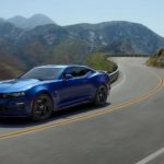 A blue 2022 Chevy Camaro ZL1 is shown driving on a highway through the mountains.