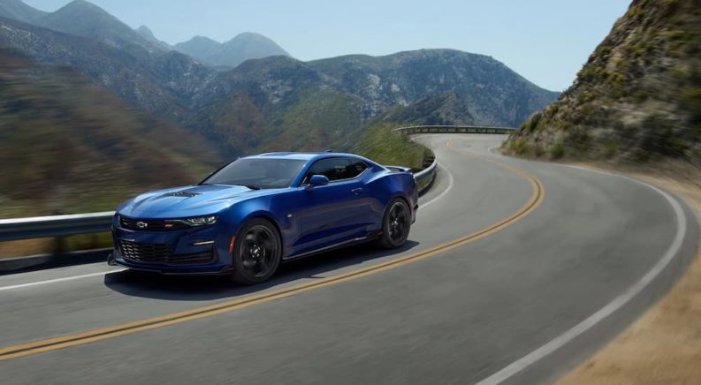 A blue 2022 Chevy Camaro ZL1 is shown driving on a highway through the mountains.