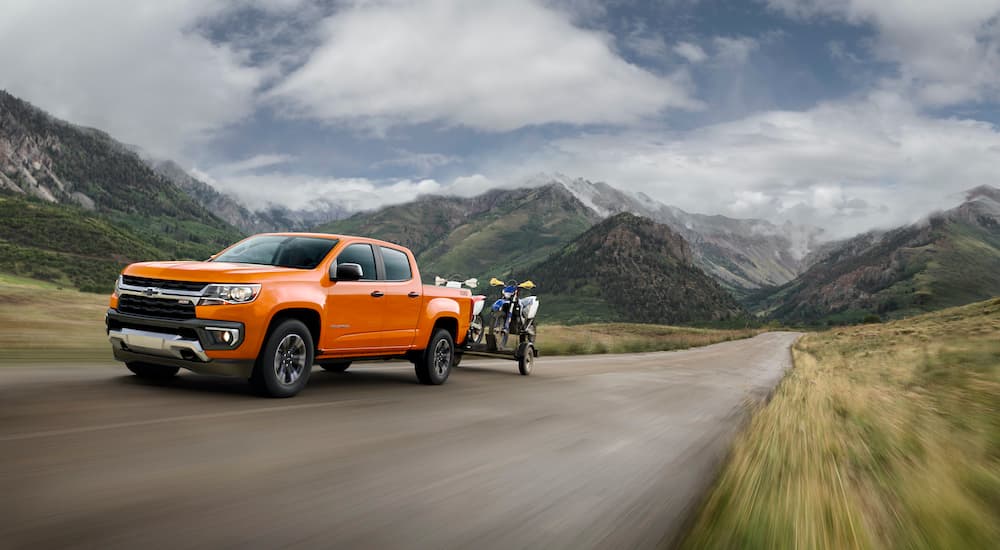 An orange 2022 Chevy Colorado is shown towing dirt-bikes on a trailer.