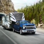 A blue 2022 Chevy Silverado 2500HD is shown towing a fifth wheel trailer through a mountainside tunnel.