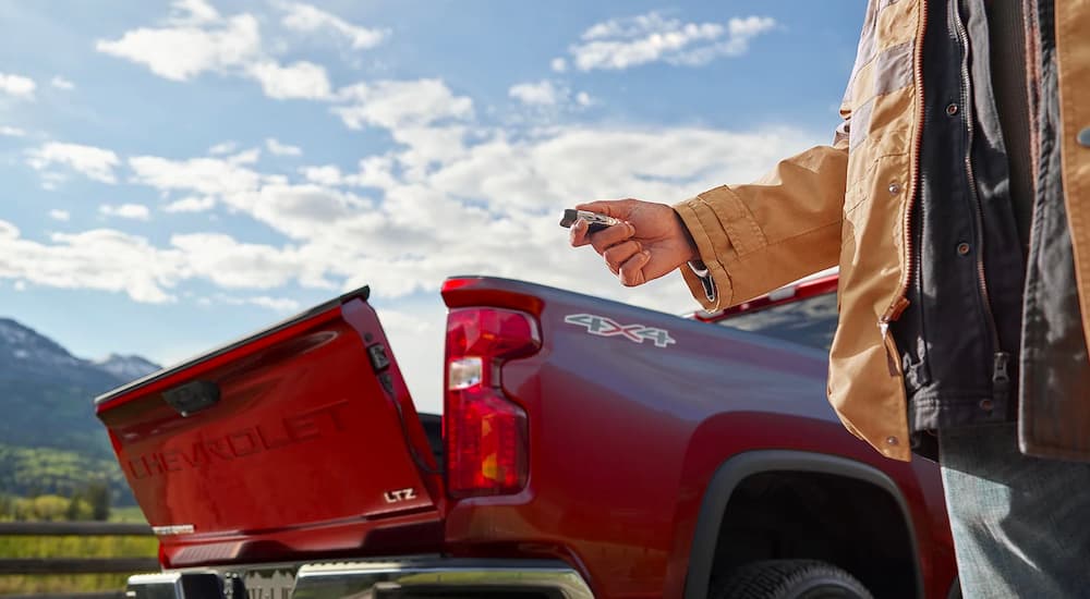 A man is shown opening the tailgate of a red 2022 Chevy Silverado HD LTZ with a keyfob.