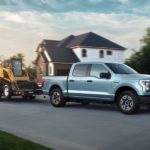 A light blue 2022 Ford F-150 Lightning is shown towing a skid-steer on a trailer.