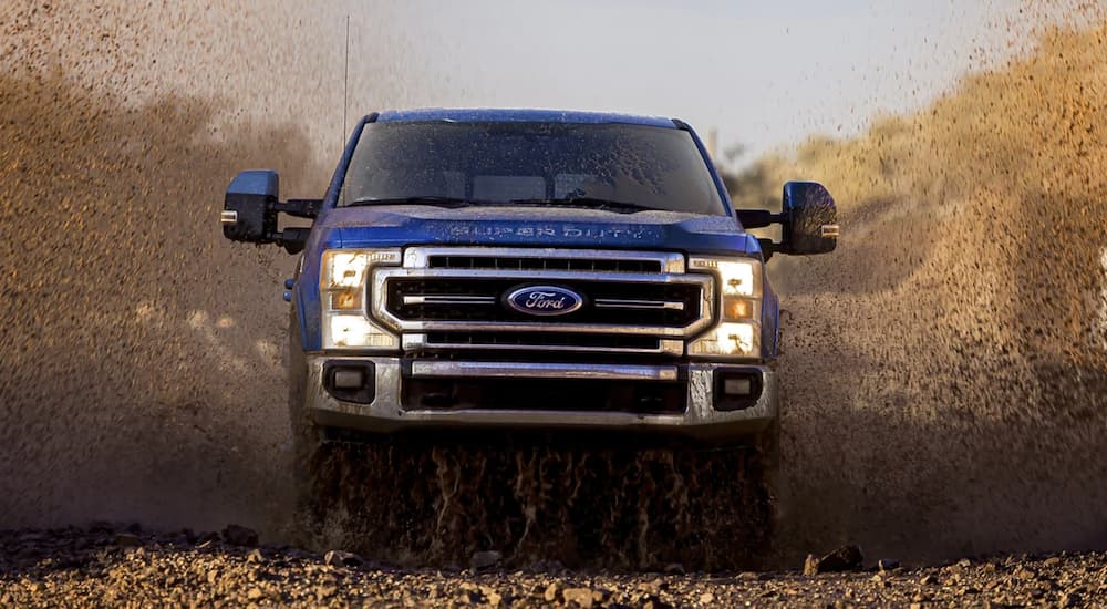 A dark blue 2022 Ford Super Duty is shown from the front off-roading through a dusty field.