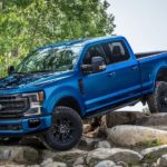 A blue 2022 Ford Super Duty is shown from the side parked on a pile of rocks in the mountains.