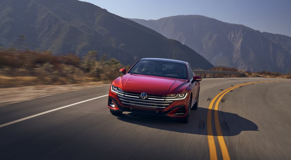 A red 2022 Volkswagen Arteon is shown from the front driving on a highway through the mountains.