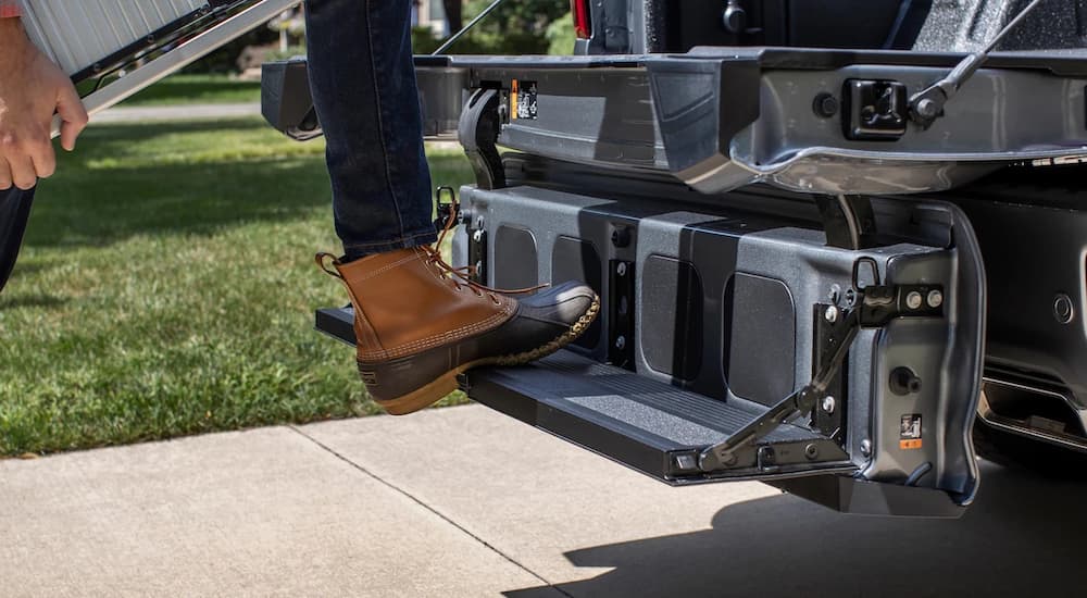 A person is shown stepping on the Multi-Flex Tailgate of a grey 2021 Chevy Silverado after visiting a Chevy dealer.